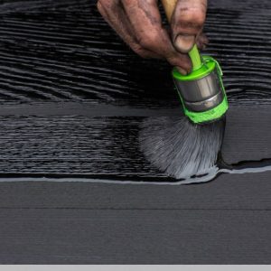 Una mano d'uomo sporca di nero impugna un pennello col quale sta trattando con olio impregnante una tavola di legno bruciato con la tecnica dello Yakisugi