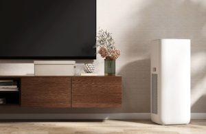 Un purificatore d'aria bianco accanto a un mobile tv con sopra un grande televisore