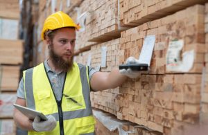Un operaio di un magazzino di legname sta controllando i codici sulle assi di legno conservate in grandi scaffali
