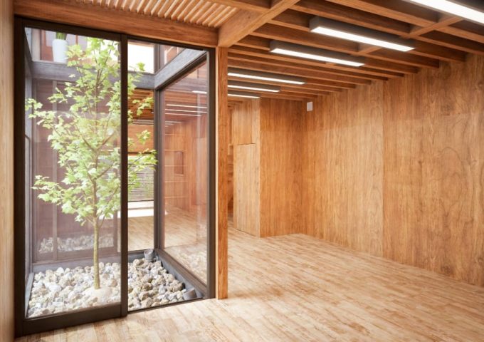 Interno non arredato e molto luminoso di una casa ecologica costruita interamente in legno, con una vetrata con pareti vetrate che danno su un mini-giardino con ciottoli di pietra e un albero