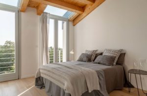 Camera da letto moderna in una stanza con parquet, soffitto con travi a vista, finestre e lucernai