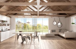 Ampio e luminoso open space a piano terra con soffitto con travi a vista in legno chiaro e parquet dello stesso colore. Nella stanza ci sono cucina, salotto e sala da pranzo in stile moderno minimale e in fondo una grande parete finestrata dà su un giardino
