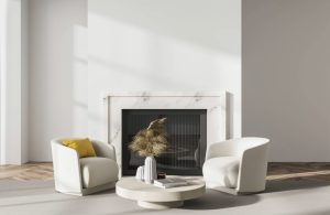Salotto minimale sui toni del bianco con caminetto rivestito in marmo, parquet a spina di pesce, tavolo da caffè circolare, tappeto chiaro e due poltrone