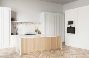 Cucina sui toni del bianco e del legno, con pareti bianche, mobili bianchi, parquet, paraschizzi in marmo bianco e isola in marmo e legno