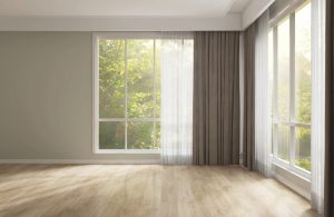 Una luminosa stanza senza mobili con pavimento in parquet e tende alle finestre