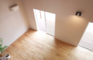 Vista dall'alto di uno spazio interno vuoto, con pareti bianche, pavimento in parquet e porte a vetri scorrevoli da cui entra luce naturale