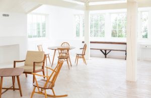 Ambiente interno luminoso con tavolini e sedie, pavimento in parquet, colonne in legno bianche come le pareti e il soffitto