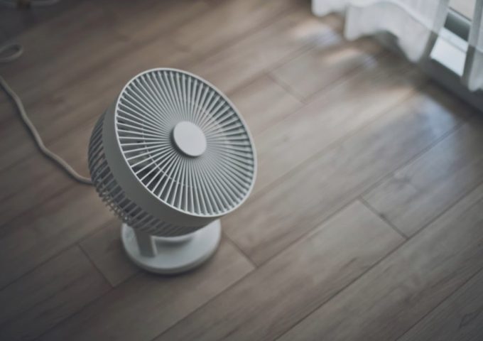 Un ventilatore poggiato su un pavimento in parquet, visto dall'alto