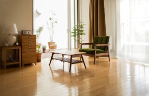 Angolo di un salotto con mobili in stile modernista, finestre con tende scure e tende bianche semitrasparenti da cui entra luce che si riflette sul parquet con finitura brillante