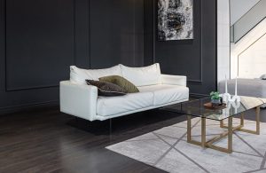 Angolo di un grande salotto con pareti grigio scuro, parquet scuro, divano bianco, tappeto chiaro, tavolino da caffè in vetro e metallo