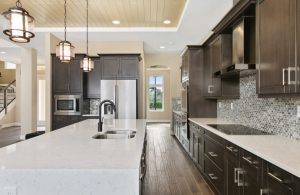Grande e luminosa cucina sui toni del beige, del bianco e del marrone scuro, con penisola, pavimento in parquet scuro, finestra che dà sul giardino e, a sinistra, scale che salgono al piano superiore