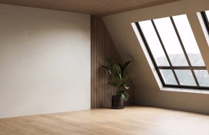 Angolo di una stanza moderna con un design minimalista. La stanza ha un pavimento in legno chiaro e una parete bianca liscia. Un'altra parete è rivestita con pannelli di legno verticali. C'è una grande finestra inclinata con cornice nera che lascia entrare molta luce naturale. Accanto alla finestra, c'è una pianta verde in un vaso nero