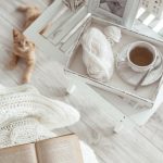 Angolo lettura shabby chic con tavolino bianco, libro e parquet grigio chiaro